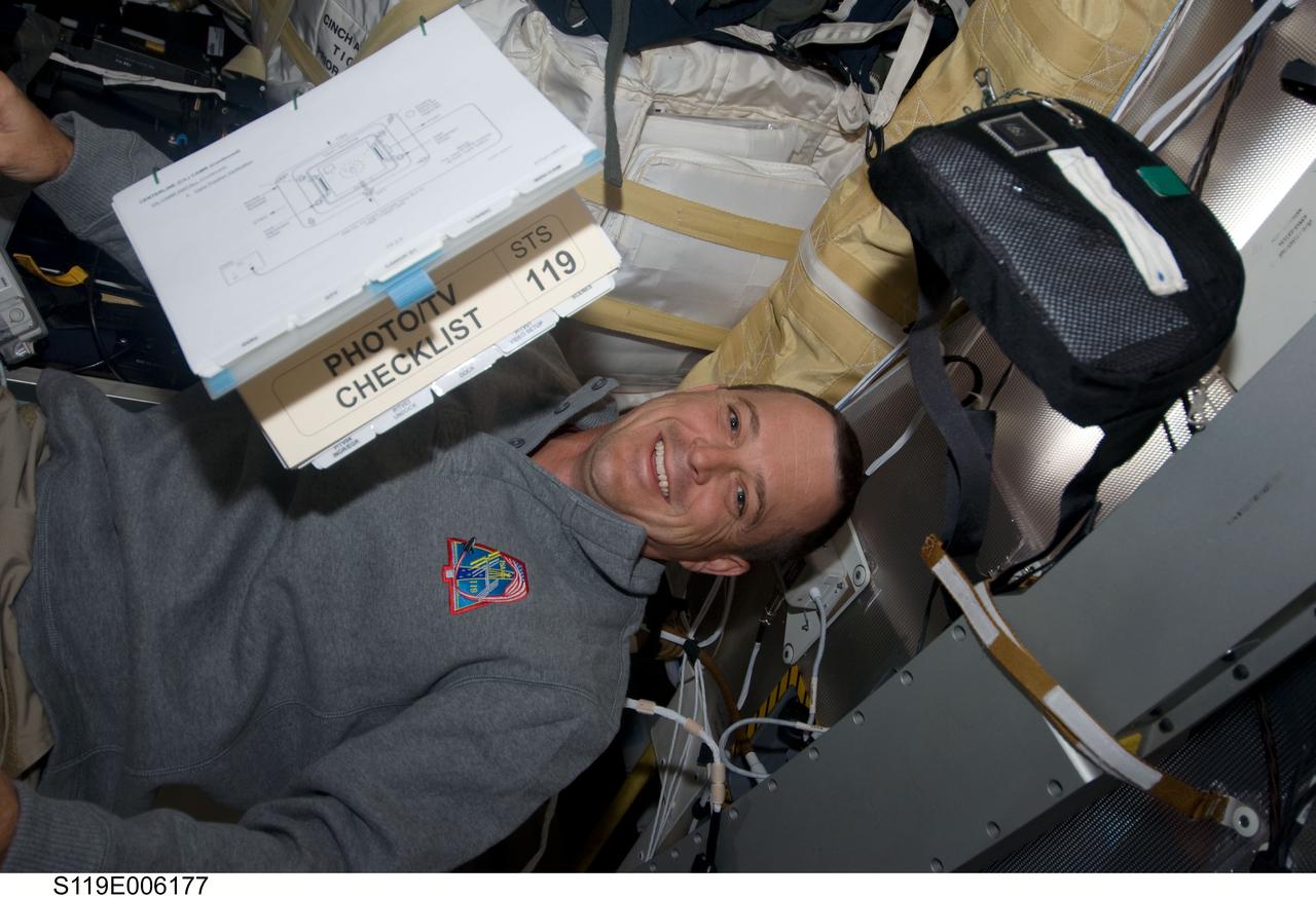 S119-E-006177 (16 March 2009) --- Astronaut Richard Arnold, STS-119 mission specialist, takes a moment for a photo while working on the middeck of Space Shuttle Discovery during flight day two activities. A procedures checklist manual floats freely near Arnold.