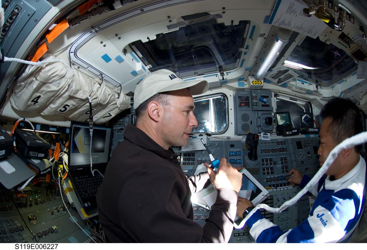S119-E-006227 (16 March 2009) --- Astronaut Lee Archambault (left), STS-119 commander, uses a communication system on the aft flight deck of Space Shuttle Discovery during flight day two activities. Japan Aerospace Exploration Agency (JAXA) astronaut Koichi Wakata, mission specialist, is at right.