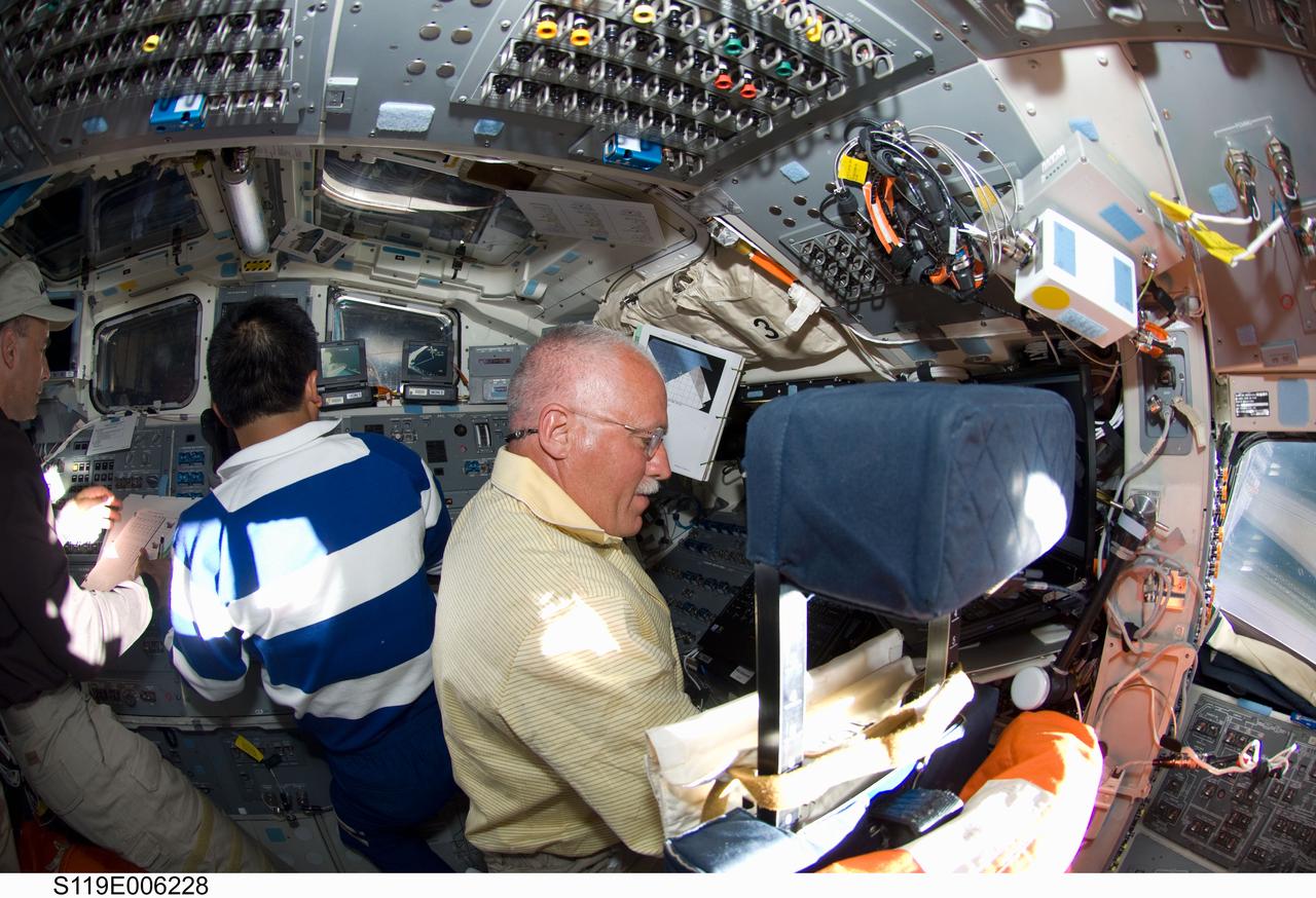 S119-E-006228 (16 March 2009) --- Astronaut John Phillips (right), Japan Aerospace Exploration Agency (JAXA) astronaut Koichi Wakata, both STS-119 mission specialists; along with astronaut Lee Archambault (partially out of frame at left), commander, work on the flight deck of Space Shuttle Discovery during flight day two activities.