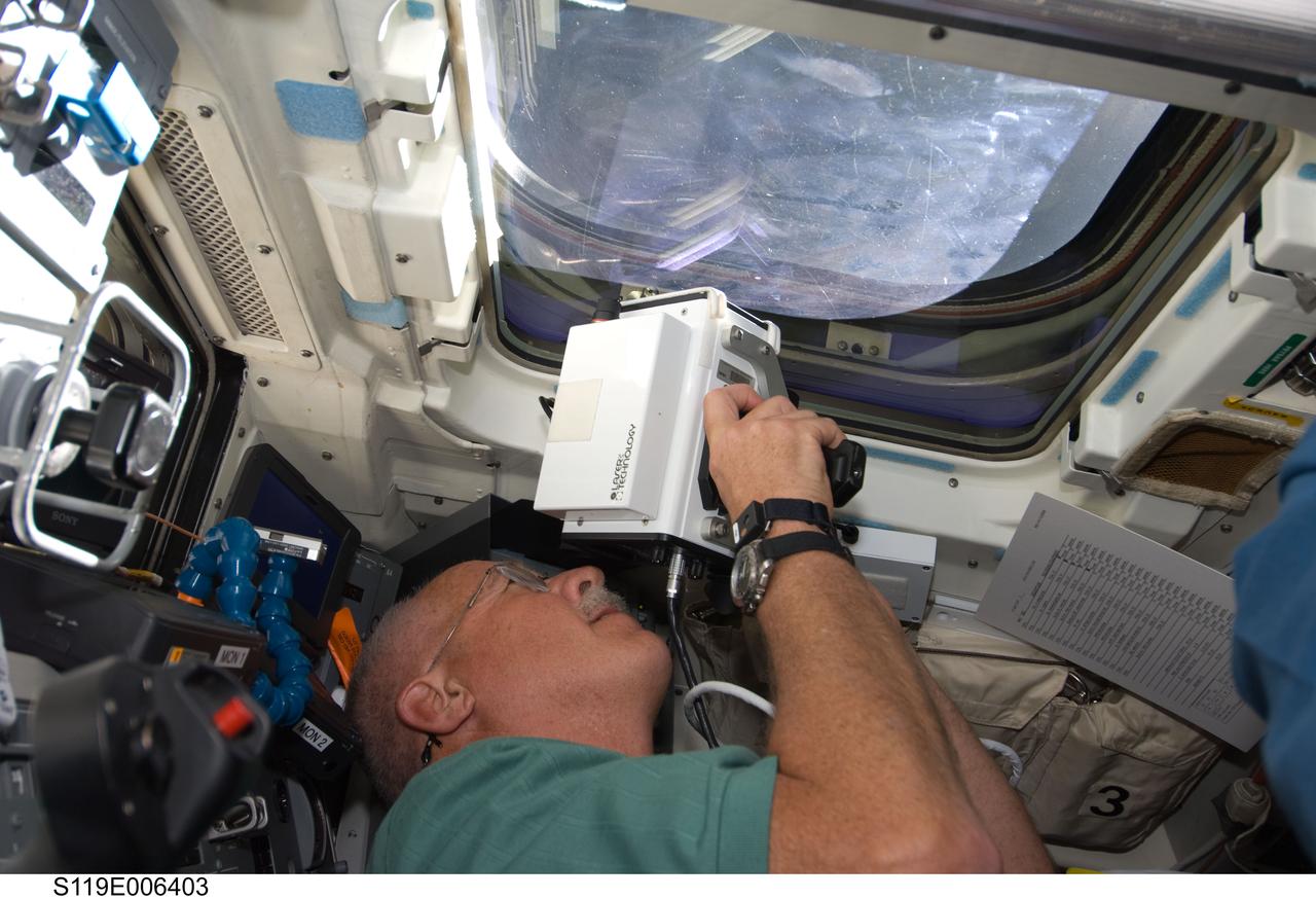 S119-E-006403 (17 March 2009) --- Astronaut John Phillips, STS-119 mission specialist, uses a handheld laser ranging device -- designed to measure the distance between two spacecraft -- through one of the overhead windows on the aft flight deck of Space Shuttle Discovery to track the range of the International Space Station during rendezvous operations.