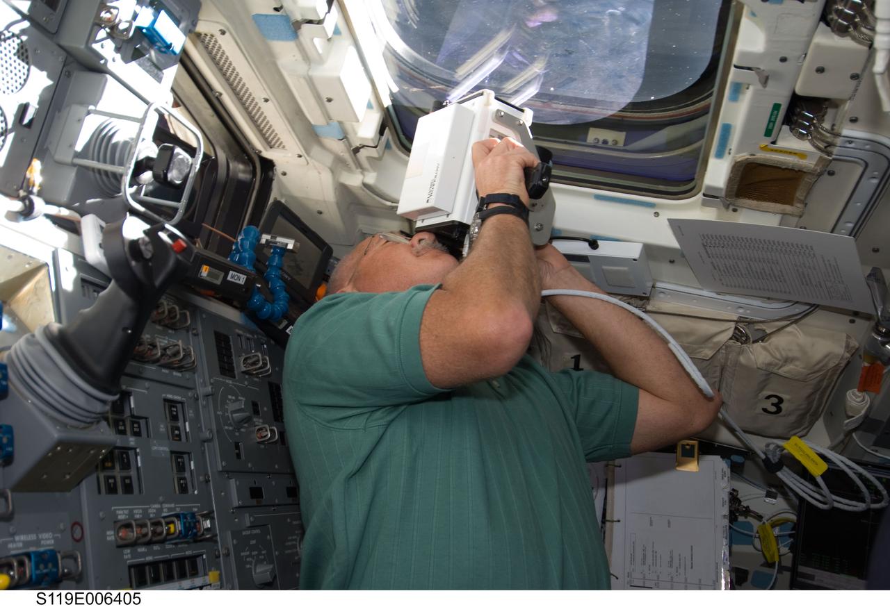S119-E-006405 (17 March 2009) --- Astronaut John Phillips, STS-119 mission specialist, aims a handheld laser ranging device -- designed to measure the distance between two spacecraft -- through one of the overhead windows on the aft flight deck of Space Shuttle Discovery to track the range of the International Space Station during rendezvous operations.