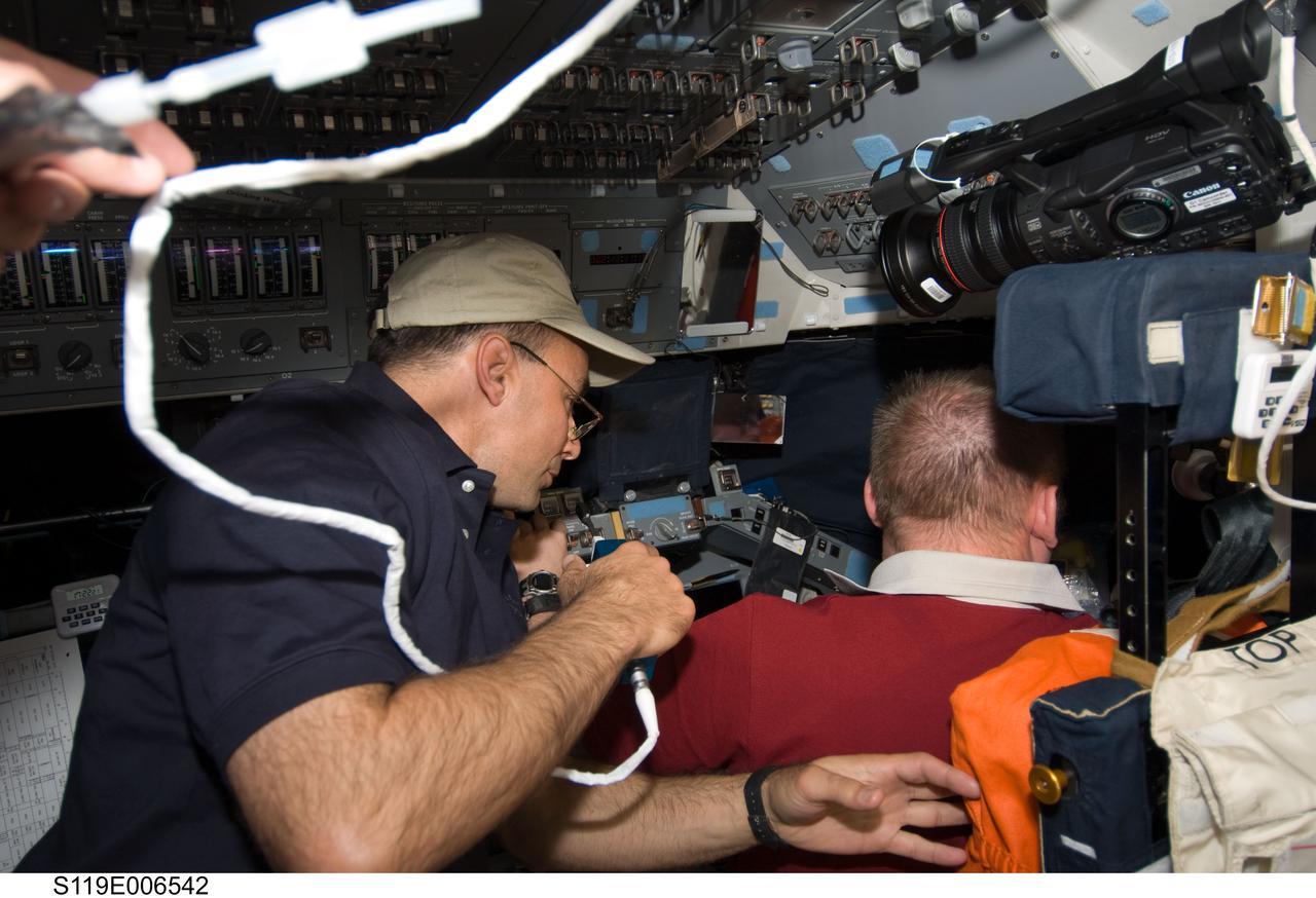 S119-E-006542 (18 March 2009) --- Astronauts Lee Archambault (left), STS-119 commander, uses a communication system on the flight deck of Space Shuttle Discovery while docked with the International Space Station. Archambault and Michael Fincke, Expedition 18 commander, are watching outside activities of the shuttle’s and station’s robotic arms as the S6 truss segment is moved from Discovery’s cargo bay.