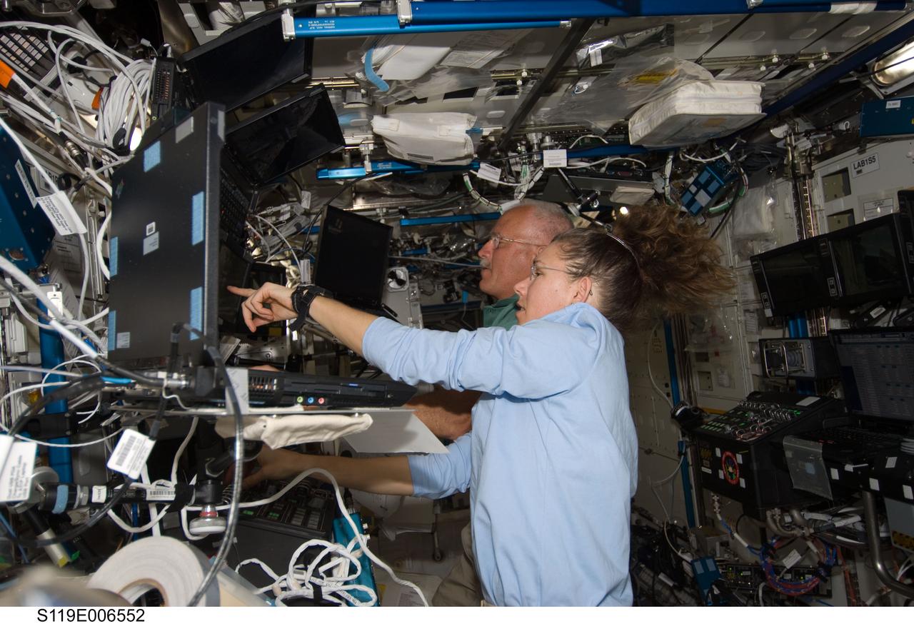 S119-E-006552 (18 March 2009) --- Astronauts John Phillips (background) and Sandra Magnus, both STS-119 mission specialists, work the controls of the station's robotic Canadarm2 in the Destiny laboratory of the International Space Station while Space Shuttle Discovery is docked with the station.