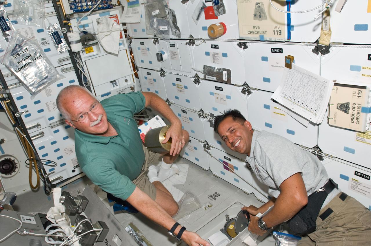 S119-E-006645 (19 March 2009) --- Astronauts John Phillips (left) and Joseph Acaba, both STS-119 mission specialists, work with the lithium hydroxide (LiOH) canisters beneath Space Shuttle Discovery's middeck while docked with the International Space Station.