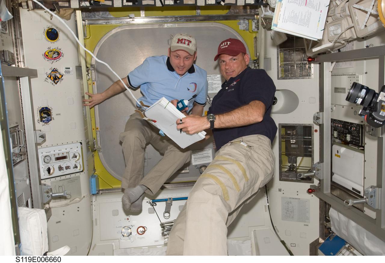S119-E-006660 (19 March 2009) --- Astronauts Michael Fincke (left), Expedition 18 commander; and Tony Antonelli, STS-119 pilot, look over procedures checklists in the Quest Airlock of the International Space Station while Space Shuttle Discovery remains docked with the station.