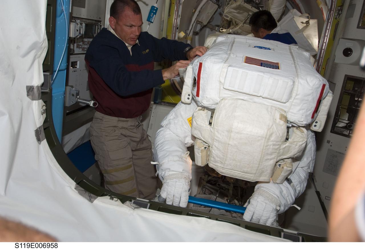 S119-E-006958 (21 March 2009) --- Astronauts Tony Antonelli (left), STS-119 pilot; and Japan Aerospace Exploration Agency’s (JAXA) Koichi Wakata (background), Expedition 18 flight engineer, assist astronauts Steve Swanson (foreground) and Joseph Acaba (totally obscured), both mission specialists, as they return to the Quest Airlock of the International Space Station as the mission’s second session of extravehicular activity (EVA) draws to a close.