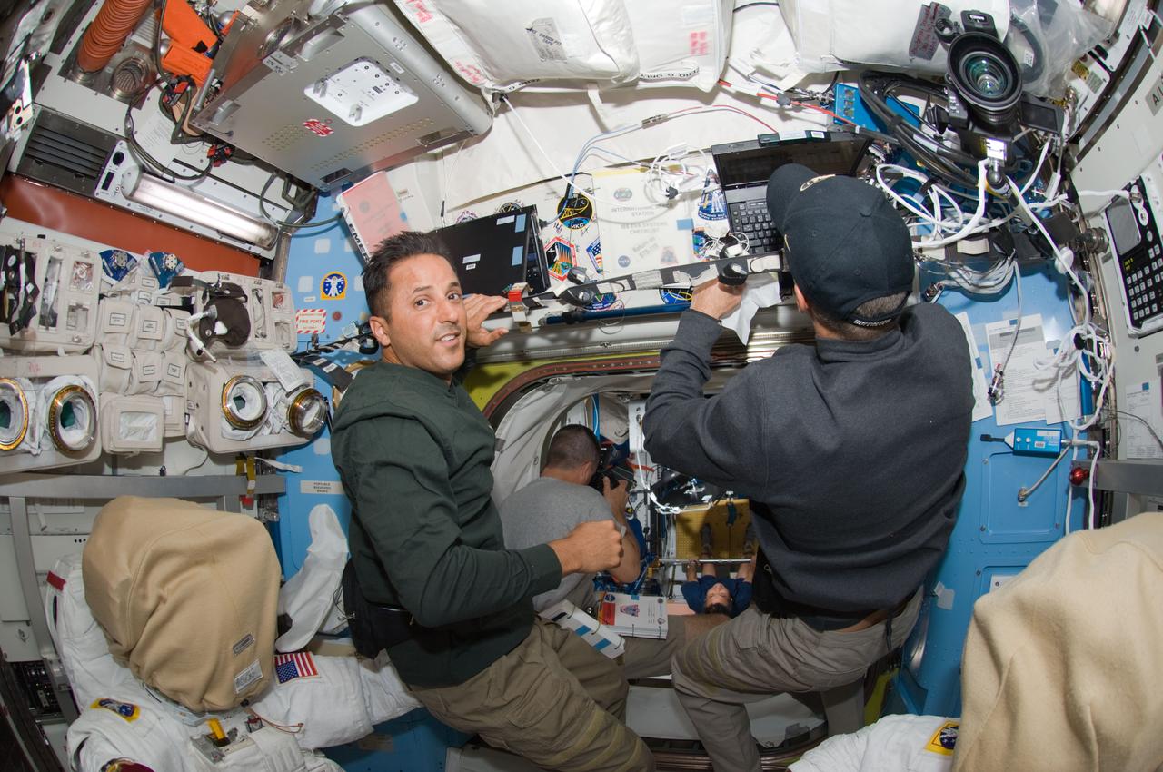 S119-E-006981 (22 March 2009) --- Astronauts Joseph Acaba (left) and Steve Swanson, both STS-119 mission specialists, work in the Quest Airlock of the International Space Station while Space Shuttle Discovery is docked with the station. Astronaut Richard Arnold (center background), mission specialist, photographs Japan Aerospace Exploration Agency (JAXA) astronaut Koichi Wakata (far background), Expedition 18 flight engineer, exercising in the Unity node.