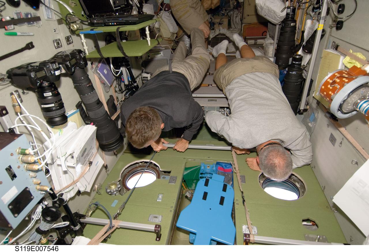 S119-E-007546 (23 March 2009) --- Astronauts Steve Swanson (left) and John Phillips, both STS-119 mission specialists, look through windows in the Zvezda Service Module of the International Space Station while Space Shuttle Discovery remains docked with the station.