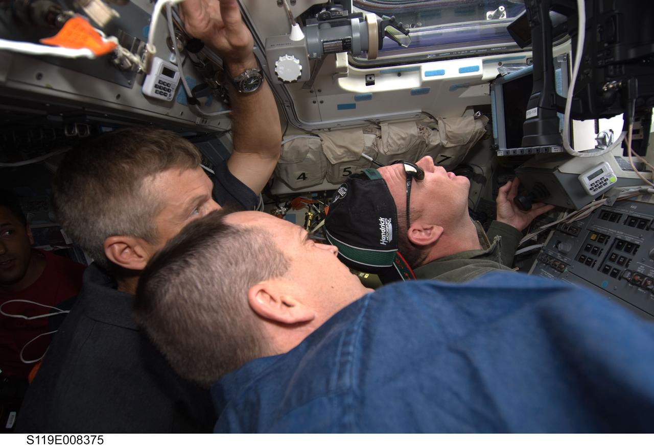 S119-E-008375 (25 March 2009) --- Astronauts Richard Arnold (foreground) and Steve Swanson, both STS-119 mission specialists; along with astronaut Lee Archambault (right), commander, look out an overhead window on the aft flight deck of the Space Shuttle Discovery after undocking from the International Space Station.