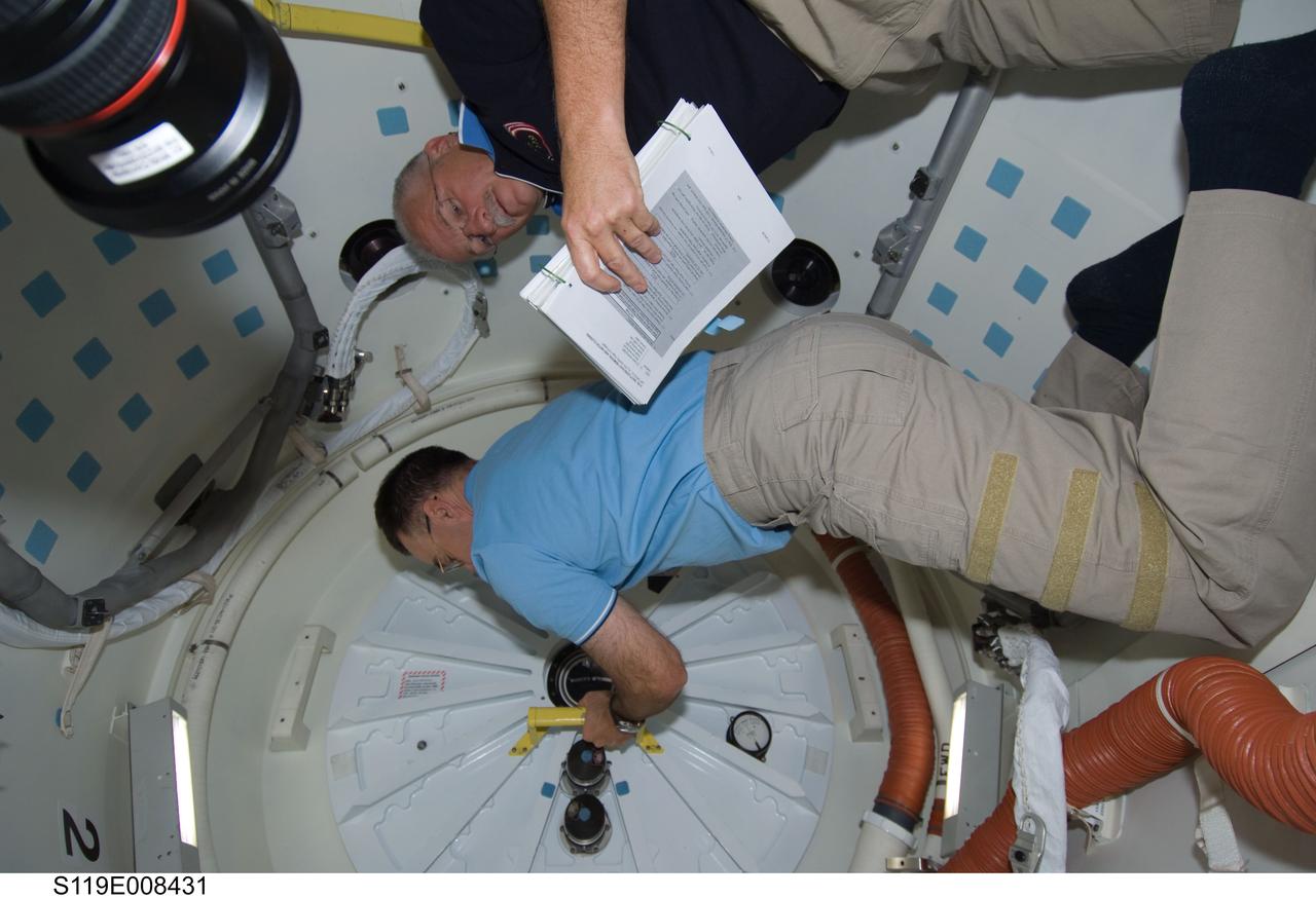 S119-E-008431(25 March 2009) --- Astronaut Lee Archambault, STS-119 commander, closes the hatch on the middeck of Space Shuttle Discovery prior to undocking from the International Space Station to conclude almost 10 days of cooperative work onboard the shuttle and the station. Astronaut John Phillips, mission specialist, looks over a procedures checklist during the activity. Undocking of the two spacecraft occurred at 2:53 p.m. (CDT) on March 25, 2009.