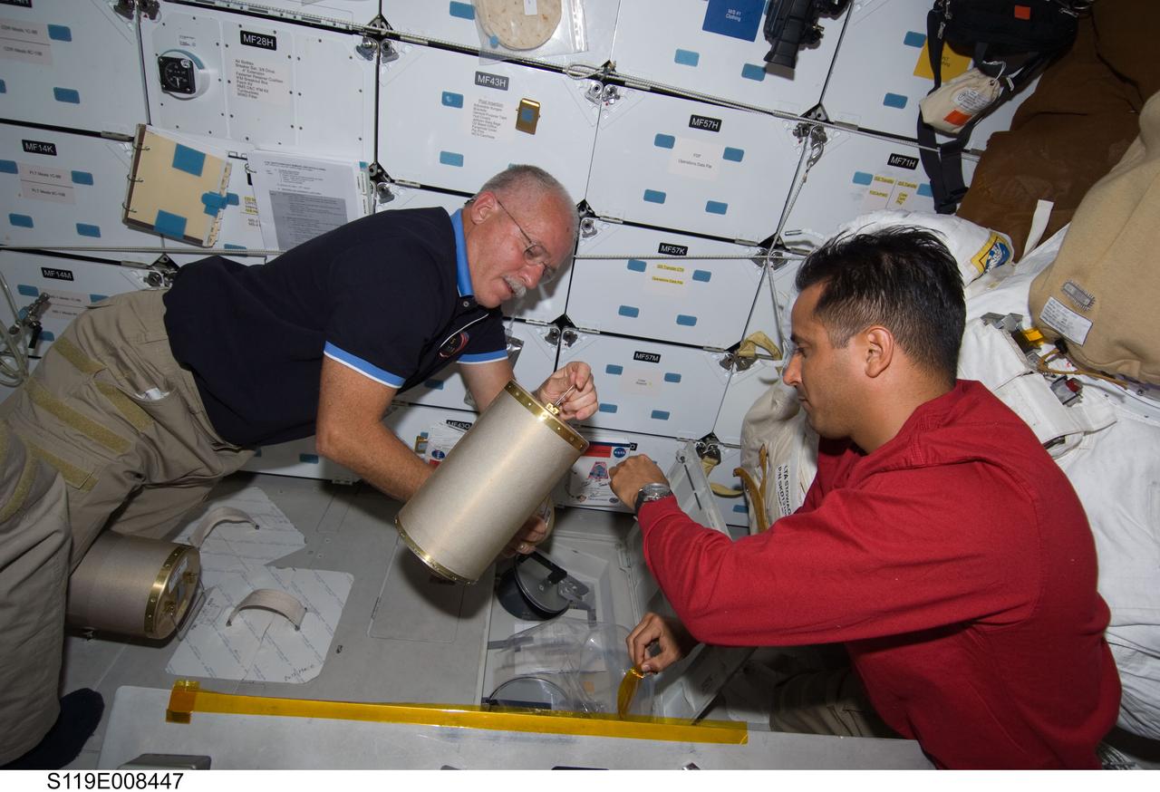 S119-E-008447 (25 March 2009) --- Astronaut John Phillips (left) and Joseph Acaba, both STS-119 mission specialists, work with the lithium hydroxide (LiOH) canisters beneath Space Shuttle Discovery's middeck during flight day 11 activities.