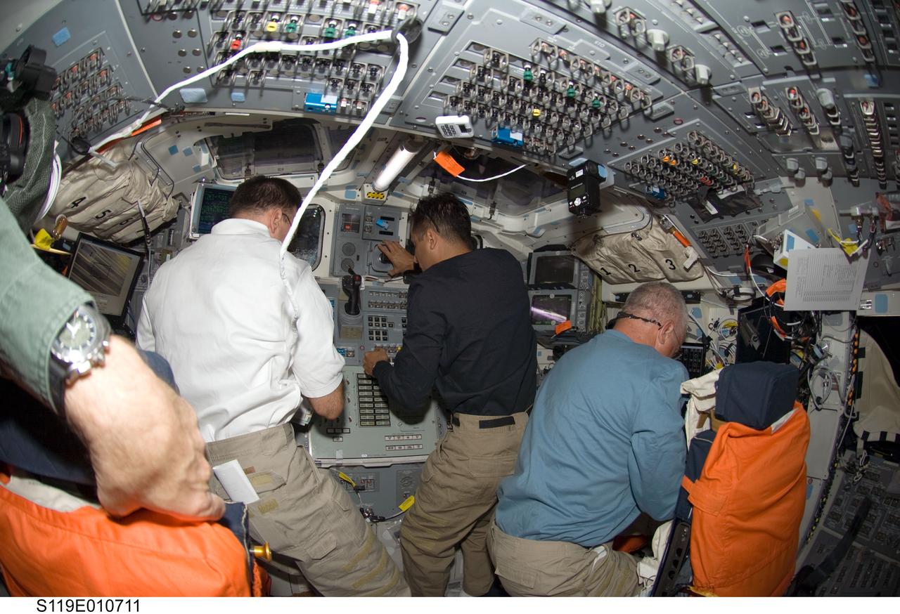 S119-E-010711 (27 March 2009) --- From left, astronaut Lee Archambault, STS-119 commander, along with astronauts Joseph Acaba and John Phillips, both mission specialists,  busy themselves with various chores on the aft deck of the Earth-orbiting Space Shuttle Discovery. The three, along with four other astronauts, are in the midst of their final full day in space before a scheduled return home on March 28.