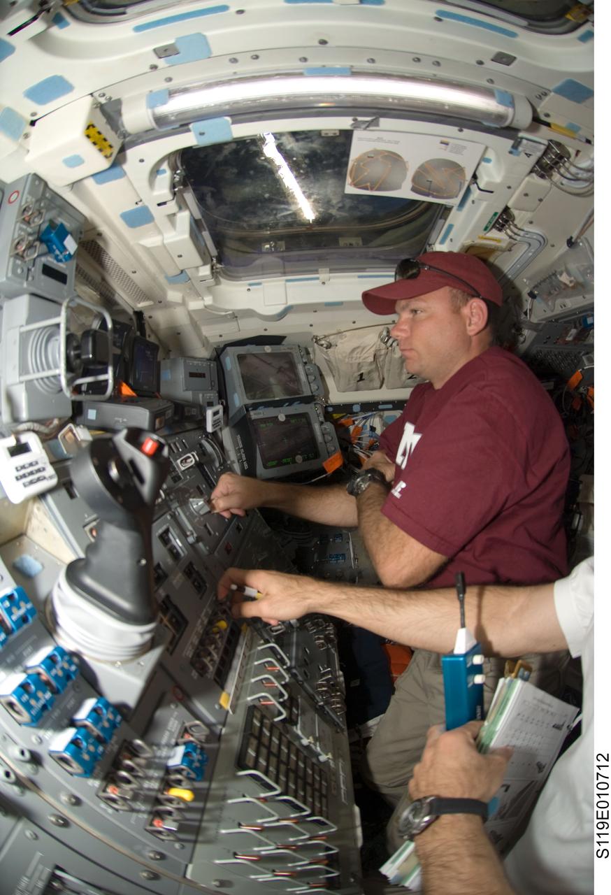 S119-E-010712 (27 March 2009) --- Astronaut Tony Antonelli, STS-119 pilot, joins a crewmate, mostly out of frame at lower right, as the two work controls on the aft flight deck of the Earth-orbiting Space Shuttle Discovery on the spacecraft's final full day in space prior to its scheduled return on March 28.