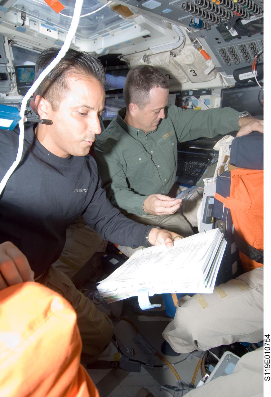 S119-E-010754 (27 March 2009) --- Astronauts Joseph Acaba, left, and  Richard Arnold, mission specialist, go over procedures check lists on the flight deck of the Earth-orbiting Space Shuttle Discovery on the spacecraft's final full day in space for STS-119.