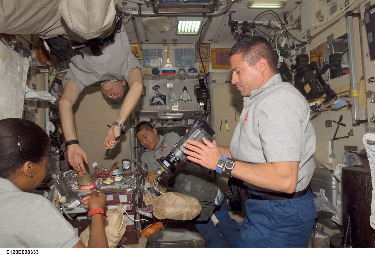 S120-E-008333 (4 Nov. 2007) --- Astronaut George Zamka (right), STS-120 pilot, uses a camera while astronauts Stephanie Wilson (left foreground), European Space Agency's (ESA) Paolo Nespoli (top), both mission specialists; and Daniel Tani, Expedition 16 flight engineer, share a meal at the galley in the Zvezda Service Module of the International Space Station while Space Shuttle Discovery is docked with the station.