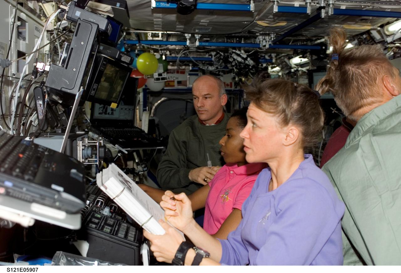S121-E-05907 (7 July 2006) --- Astronaut Lisa M. Nowak (foreground), STS-121 mission specialist, refers to a procedures checklist as astronaut Stephanie D. Wilson (center), mission specialist, works with the Mobile Service System (MSS) and Canadarm2 controls in the Destiny laboratory of the International Space Station while Space Shuttle Discovery was docked to the station. Wilson used the station's arm to move the Italian-built Leonardo Multi-Purpose Logistics Module (MPLM) from the shuttle cargo bay to install on the station's Unity node. Astronaut Jeffrey N. Williams (background), Expedition 13 NASA space station science officer and flight engineer, assisted Wilson. The MPLM was successfully latched in place by 7:15 a.m. (CDT) on July 7, 2006.