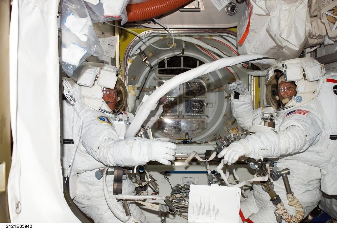 S121-E-05942 (8 July 2006) --- Astronauts Piers J. Sellers (right) and Michael E. Fossum, STS-121 mission specialists, attired in their Extravehicular Mobility Unit (EMU) spacesuits, prepare for the start of the first scheduled session of extravehicular activity (EVA) in the Quest Airlock of the International Space Station.