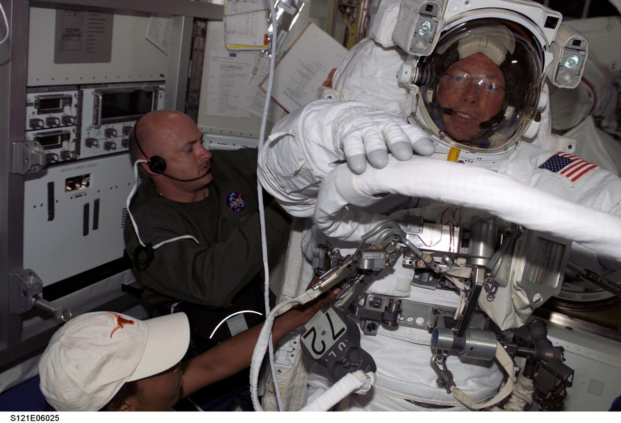 S121-E-06025 (8 July 2006) --- Astronauts Mark E. Kelly, STS-121 pilot, and Stephanie D. Wilson (partially out of frame), mission specialist, assist astronaut Michael E. Fossum, mission specialist, with the donning of his Extravehicular Mobility Unit (EMU) spacesuit in the Quest Airlock of the International Space Station prior to the start of the mission's first scheduled session of extravehicular activity (EVA).