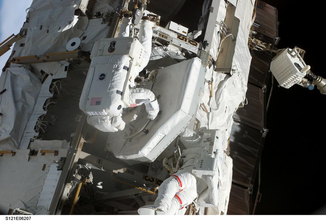 S121-E-06207 (10 July 2006) --- While anchored on the mobile foot restraint on the Canadarm2, astronaut Michael E. Fossum (left), STS-121 mission specialist, removes the trailing umbilical system-reel assembly (TUS-RA) from the S0 truss on the International Space Station during the mission's second session of extravehicular activity (EVA). Astronaut Piers J. Sellers, mission specialist, assisted Fossum by checking the clearance of the TUS-RA as it was lifted from the bay.