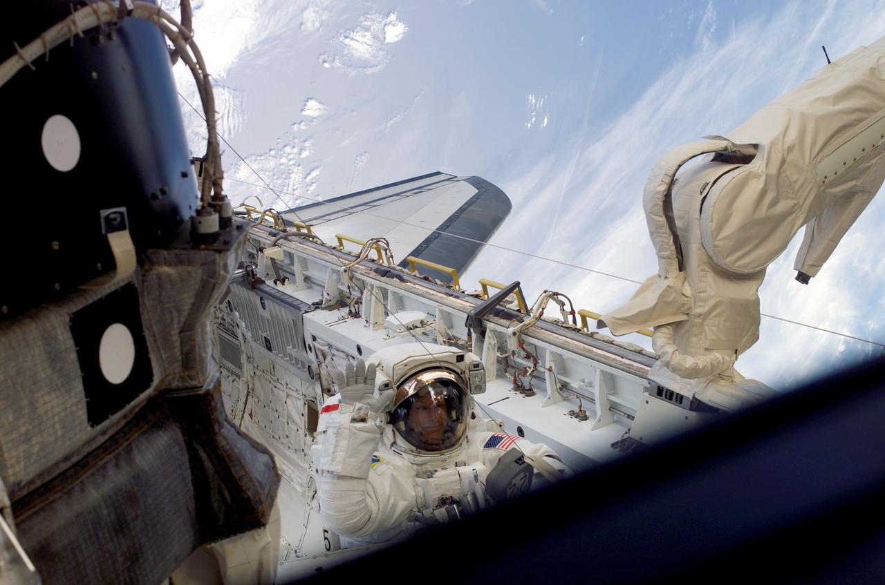 S121-E-06216 (10 July 2006) --- Astronaut Piers J. Sellers, STS-121 mission specialist, waves to a crewmate inside the Space Shuttle Discovery as he works in the shuttle's cargo bay during the mission's second session of extravehicular activity (EVA). During today's six-hour 47-minute spacewalk, Sellers and astronaut Michael E. Fossum (out of frame), mission specialist, restored the International Space Station's Mobile Transporter rail car to full operation and delivered a spare pump module for the station's cooling system.