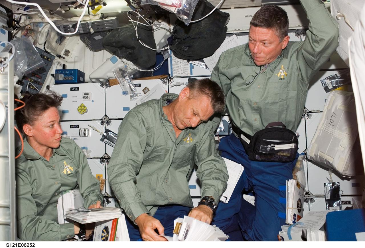 S121-E-06252 (9 July 2006) --- Astronauts Lisa M. Nowak (left), Piers J. Sellers and Michael E. Fossum, all STS-121 mission specialists, look over procedures checklists on the middeck of the Space Shuttle Discovery while docked with the International Space Station.