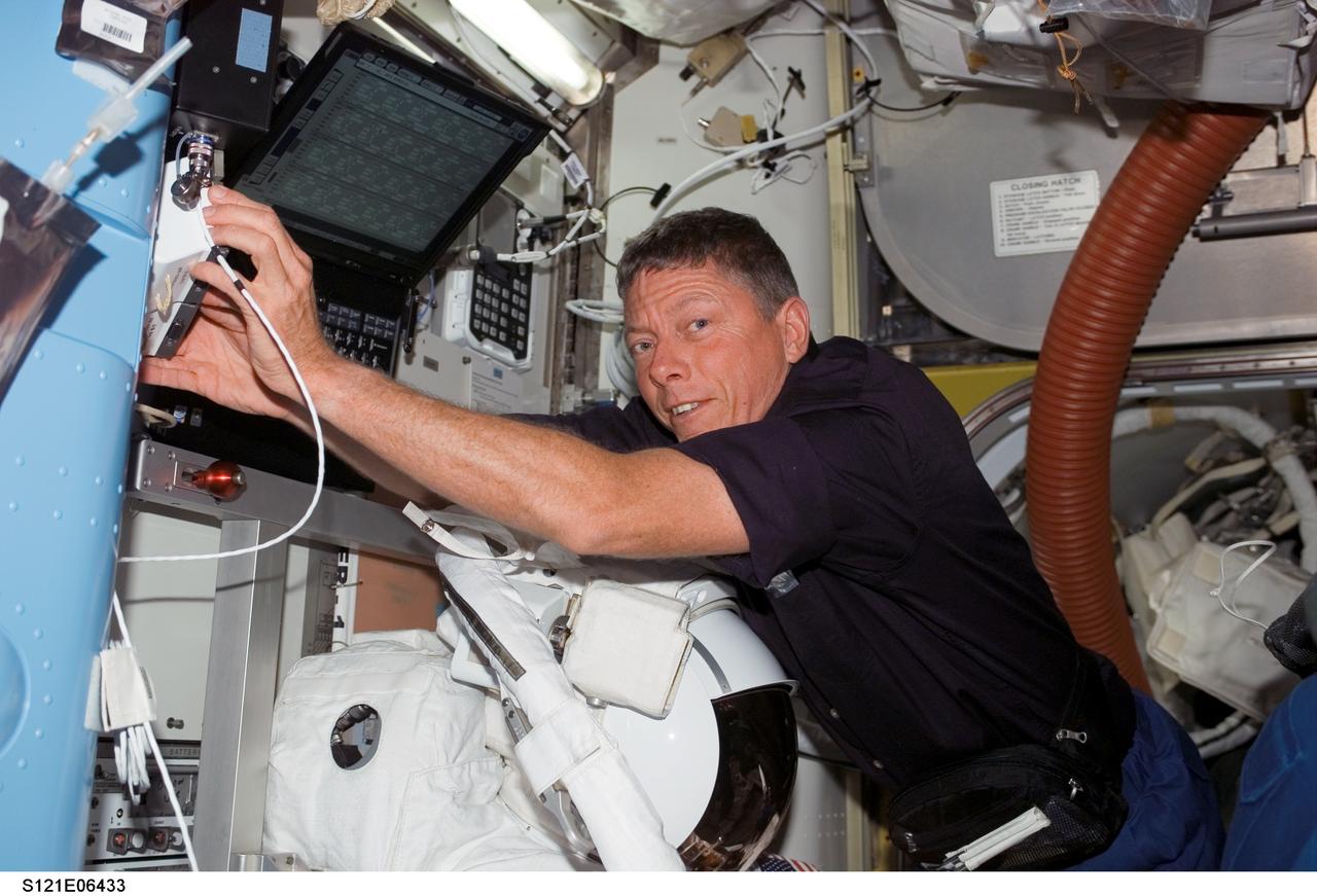 S121-E-06433 (11 July 2006) --- Astronaut Michael E. Fossum, STS-121 mission specialist, works in the Quest Airlock of the International Space Station while Space Shuttle Discovery was docked with the station. An Extravehicular Mobility Unit (EMU) spacesuit is visible at bottom.
