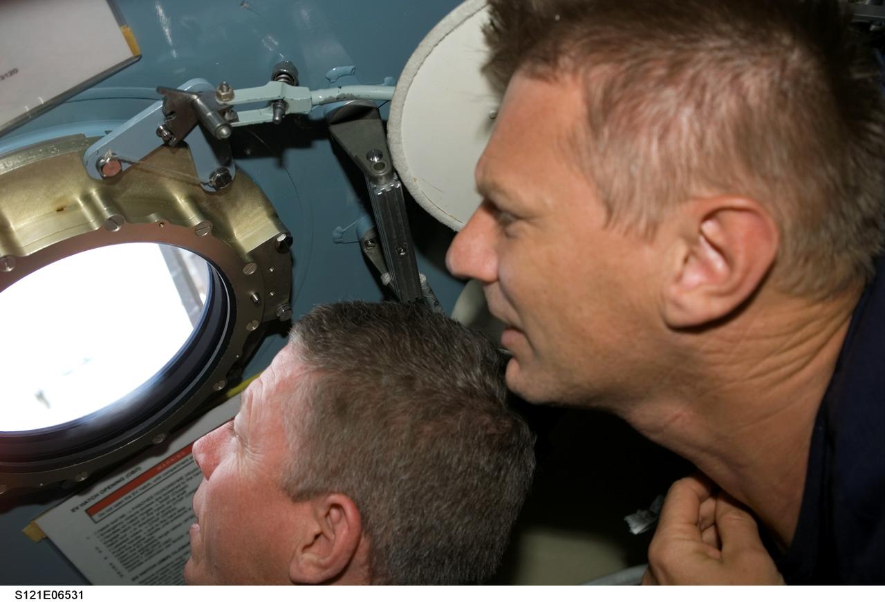 S121-E-06531 (13 July 2006) --- Astronauts Michael E. Fossum (left) and Piers J. Sellers, both STS-121 mission specialists, look out a window in the Pirs Docking Compartment of the International Space Station while Space Shuttle Discovery was docked with the station.