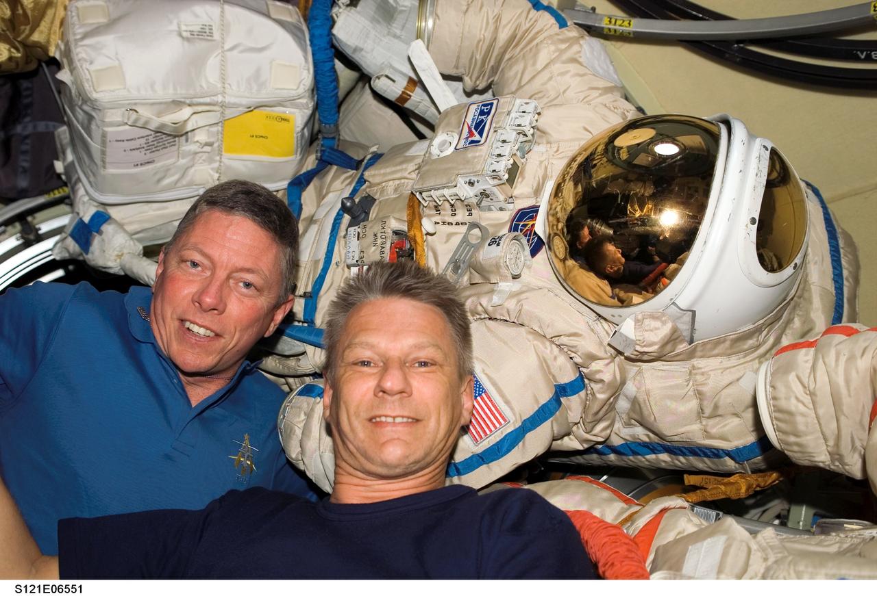 S121-E-06551 (13 July 2006) -- Astronauts Michael E. Fossum (left) and Piers J. Sellers, both STS-121 mission specialists, pose for a photo near a Russian Orlan space suit in the Pirs Docking Compartment of the International Space Station while Space Shuttle Discovery was docked with the station.