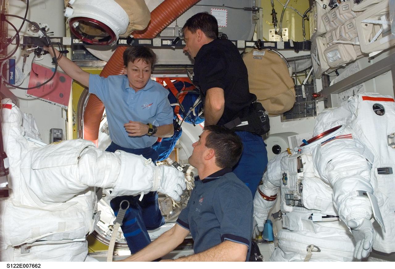 S122-E-007662 (10 Feb. 2008) --- Astronauts Peggy Whitson, Expedition 16 commander; Stanley Love and Rex Walheim (bottom), both STS-122 mission specialists, work in the Quest Airlock of the International Space Station while Space Shuttle Atlantis is docked with the station. Two Extravehicular Mobility Unit (EMU) spacesuits are visible in the image.