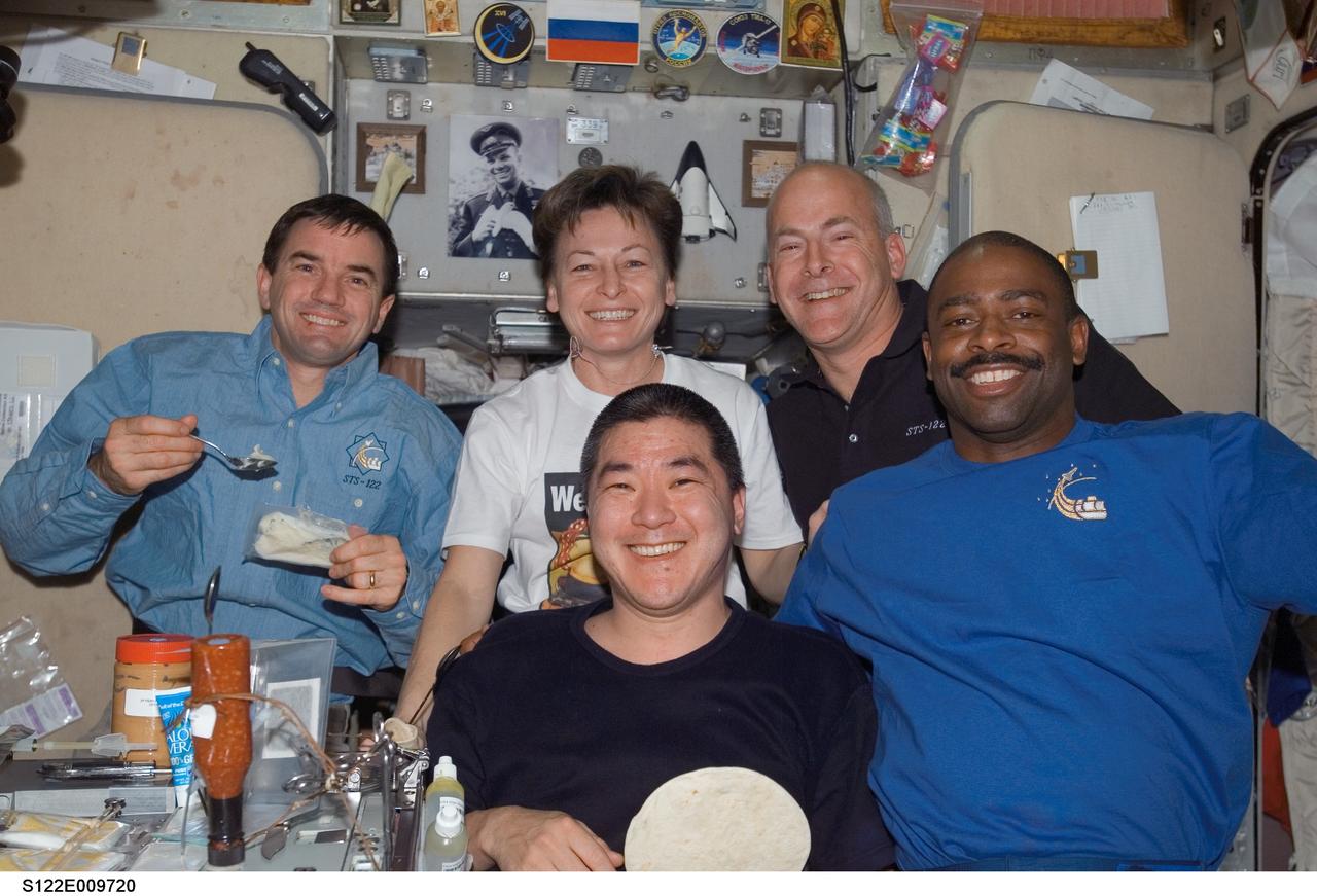 S122-E-009720 (17 Feb. 2008) --- STS-122 and Expedition 16 crewmembers share a meal at the galley in the Zvezda Service Module of the International Space Station. Pictured from the left (foreground) are NASA astronauts Daniel Tani and Leland Melvin, both STS-122 mission specialists. Pictured from the left (back row) are NASA astronauts Rex Walheim, STS-122 mission specialist; Peggy Whitson, Expedition 16 commander; and Alan Poindexter, STS-122 pilot.