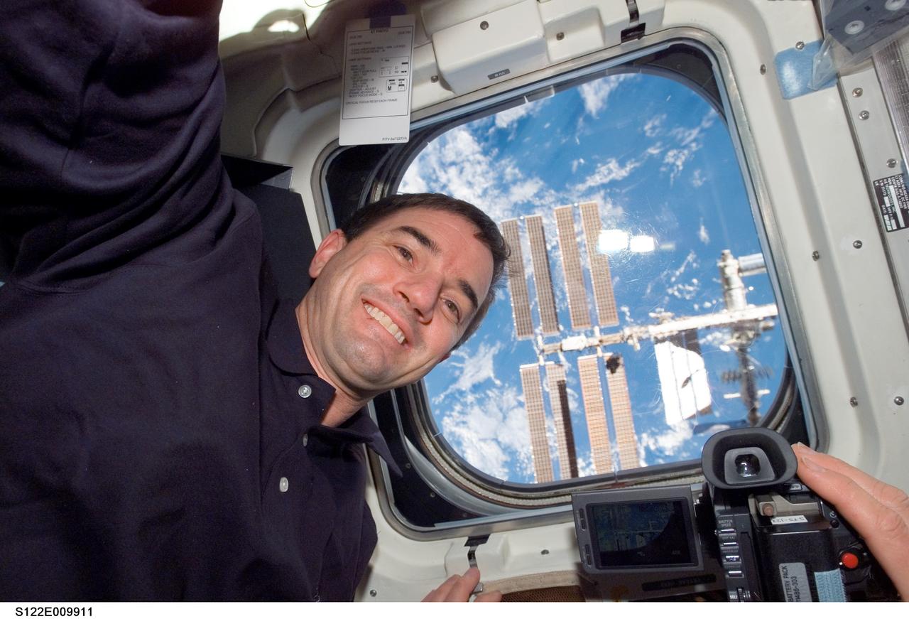 S122-E-009911 (18 Feb. 2008) --- Astronaut Rex Walheim, STS-122 mission specialist, poses for a photo near a window on the aft flight deck of Space Shuttle Atlantis shortly after undocking from the International Space Station, which is visible through the window.
