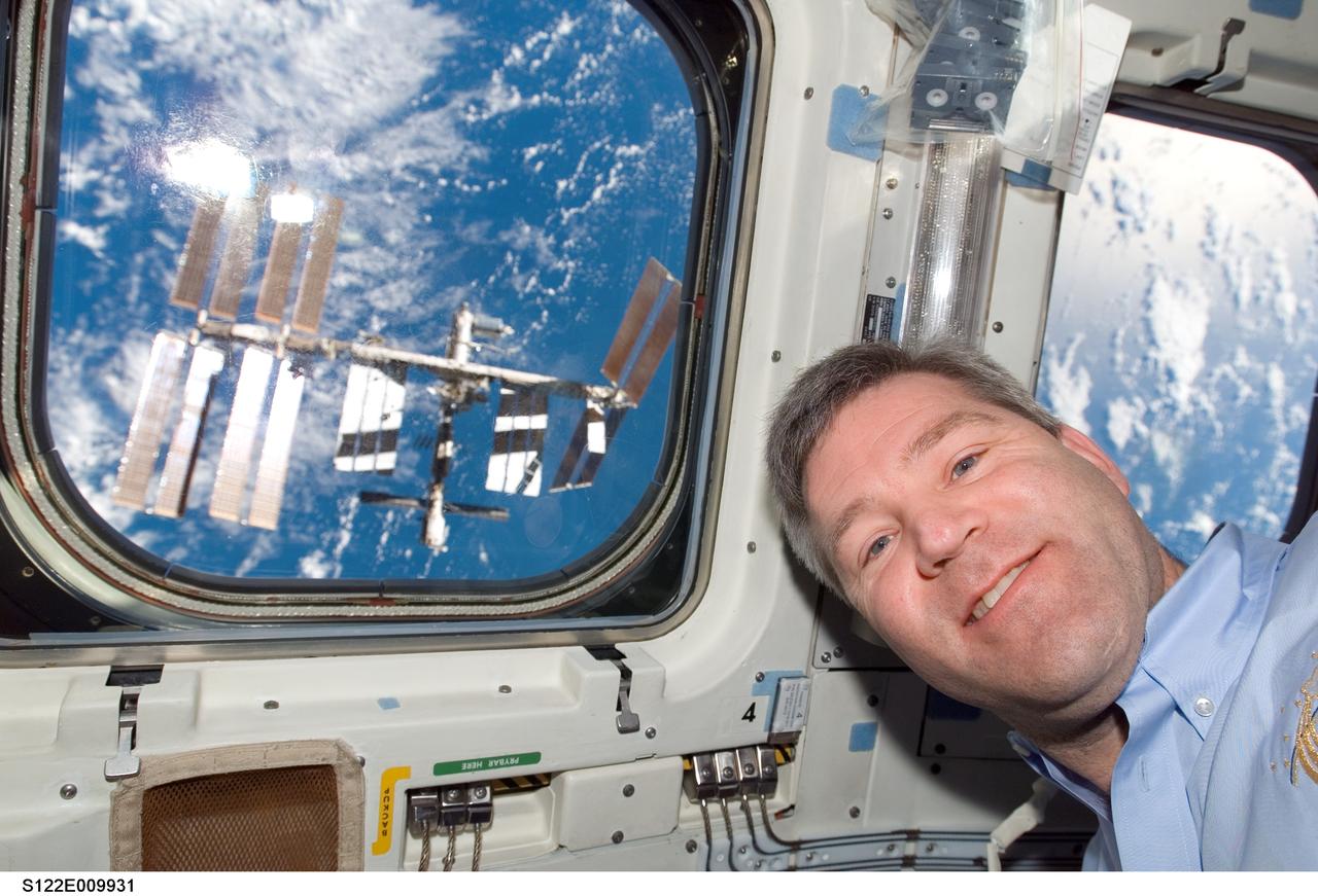 S122-E-009931 (18 Feb. 2008) --- Astronaut Steve Frick, STS-122 commander, poses for a photo near a window on the aft flight deck of Space Shuttle Atlantis shortly after undocking from the International Space Station, which is visible through the window.