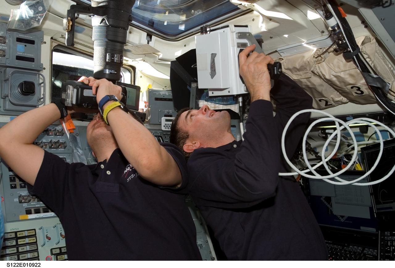 S122-E-010922 (18 Feb. 2008) --- Astronaut Rex Walheim (right), STS-122 mission specialist, uses a handheld laser ranging device -- designed to measure the range between two spacecraft -- through one of the overhead windows on the aft flight deck of Space Shuttle Atlantis after undocking from the International Space Station. Astronaut Daniel Tani, mission specialist, uses a still camera to photograph the station in its new configuration.