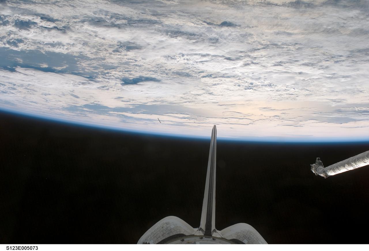 S123-E-005073 (11 Mar. 2008) --- This view out the aft windows on Endeavour's flight deck was one of a series of images recorded by the STS-123 crewmembers during their first full day in space. The end of the Canadian-built remote manipulator system's robot arm (right edge) along with the shuttle's vertical stabilizer and its two orbital maneuvering system (OMS) pods are visible. A heavily cloud-covered area of Earth fills the top half of the frame.