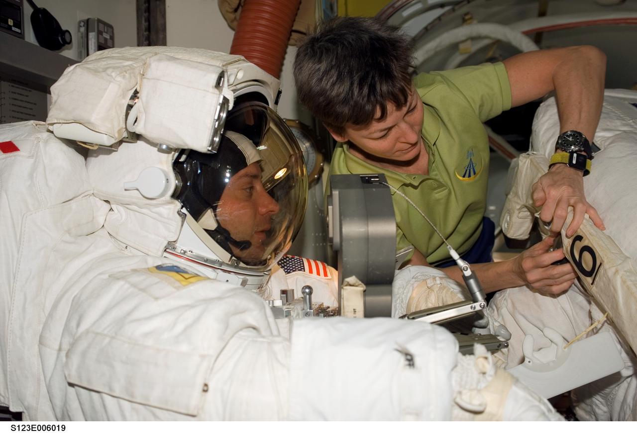 S123-E-006019 (14 March 2008) --- Astronaut Peggy Whitson, Expedition 16 commander, assists astronauts Garrett Reisman, Expedition 16 flight engineer, and Rick Linnehan (partially out of frame), STS-123 mission specialist, in doffing their Extravehicular Mobility Unit (EMU) spacesuits in the Quest Airlock of the International Space Station as the mission's first session of extravehicular activity (EVA) draws to a close.