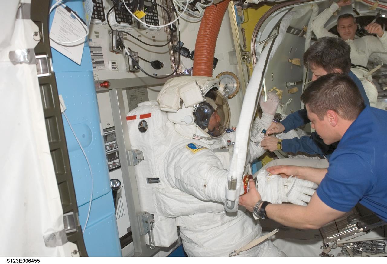 S123-E-006455 (16 March 2008) --- Astronauts Mike Foreman (left) and Rick Linnehan (background), both STS-123 mission specialists, are pictured in the Quest Airlock of the International Space Station as the mission's second session of extravehicular activity (EVA) draws to a close. Astronauts Peggy Whitson, Expedition 16 commander, and Robert L. Behnken, STS-123 mission specialist, assist the crewmembers with the doffing of the spacesuits.