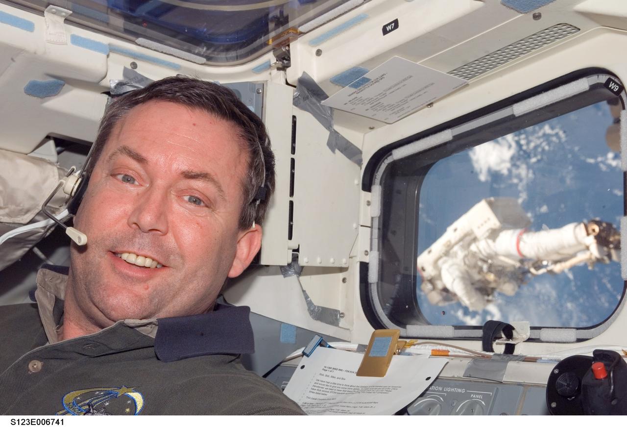 S123-E-006741 (17/18 March 2008) --- Astronaut Mike Foreman, STS-123 mission specialist, takes a brief moment for a photo on the aft flight deck of Space Shuttle Endeavour while docked with the International Space Station. Anchored to a Canadarm2 mobile foot restraint, astronaut Rick Linnehan (visible through a nearby window), mission specialist, participates in the mission's third session of extravehicular activity (EVA).