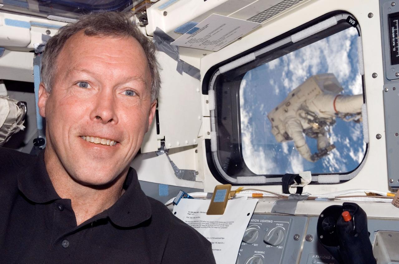 S123-E-006743 (17/18 March 2008) --- Astronaut Dominic Gorie, STS-123 commander, takes a brief moment for a photo on the aft flight deck of Space Shuttle Endeavour while docked with the International Space Station. Anchored to a Canadarm2 mobile foot restraint, astronaut Rick Linnehan (visible through a nearby window), mission specialist, participates in the mission's third session of extravehicular activity (EVA).