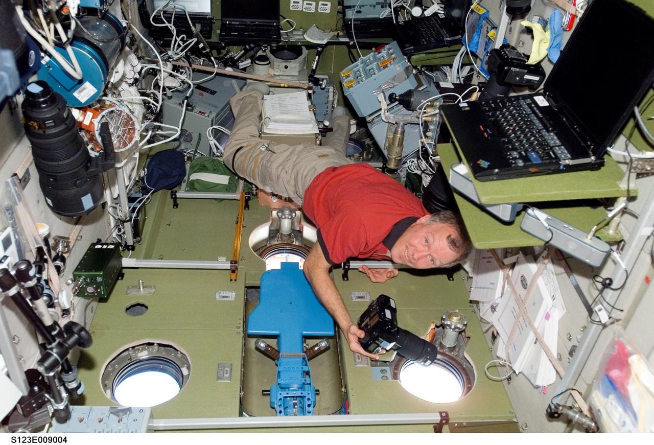 S123-E-009004 (23 March 2008) --- Astronaut Dominic Gorie, STS-123 commander, uses a still camera at a window in the Zvezda Service Module of the International Space Station while Space Shuttle Endeavour is docked with the station.