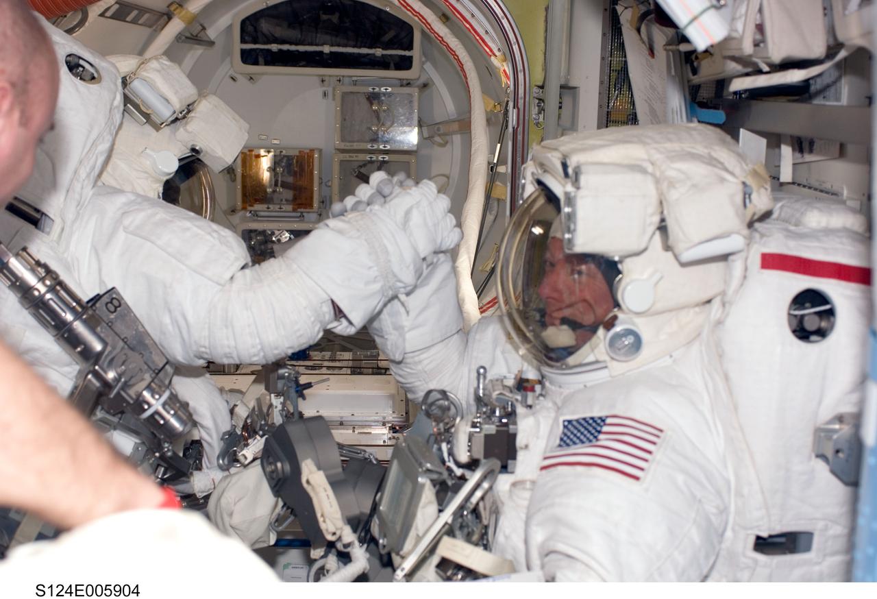 S124-E-005904 (3 June 2008) --- Attired in their Extravehicular Mobility Unit (EMU) spacesuits, astronauts Mike Fossum (right) and Ron Garan, STS-124 mission specialists, interlock hands in the Quest Airlock of the International Space Station as they are about to begin the mission's first scheduled spacewalk while Space Shuttle Discovery is docked with the station.