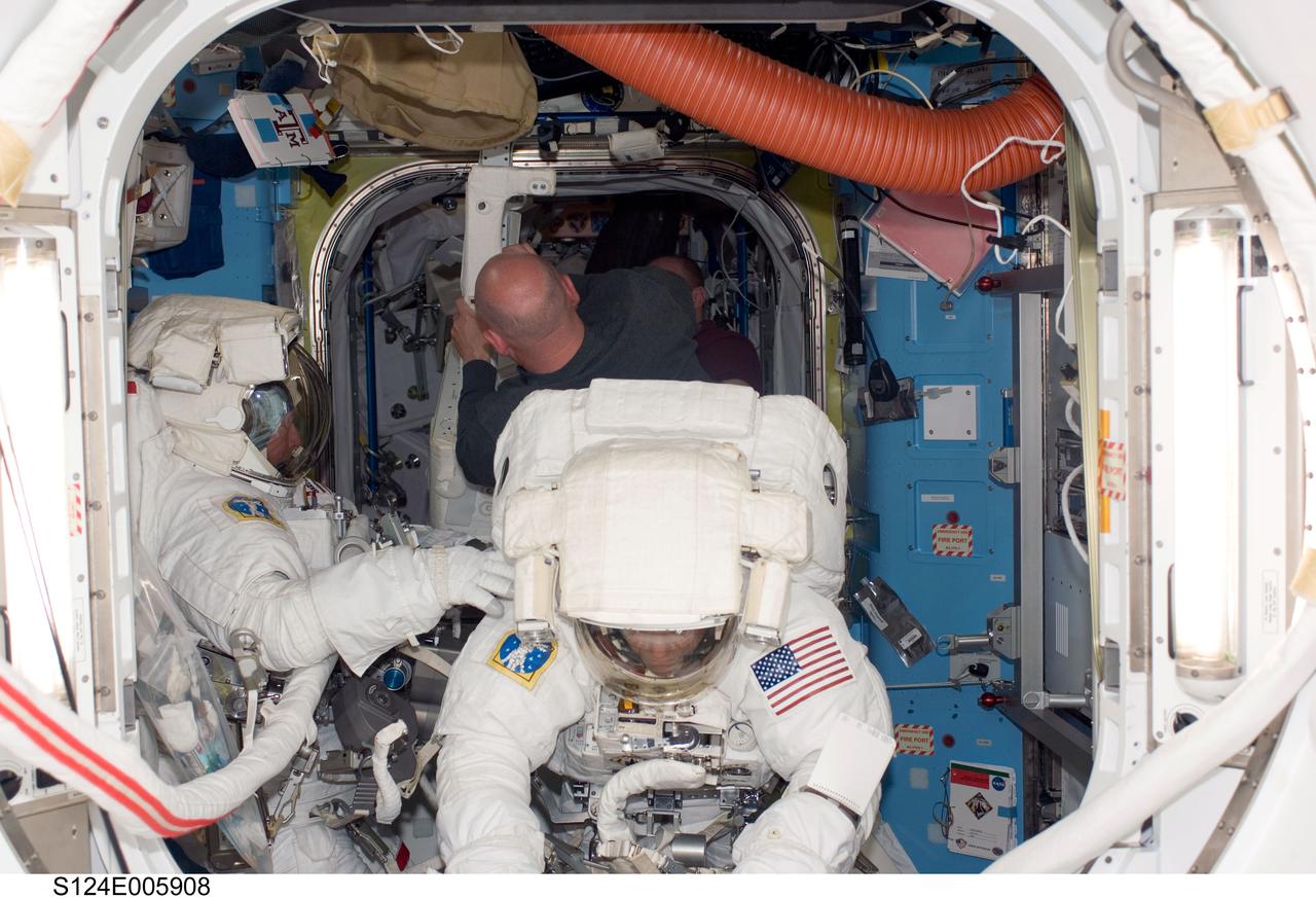 Attired in their Extravehicular Mobility Unit (EMU) spacesuits, astronauts Mike Fossum (right) and Ron Garan, STS-124 mission specialists, are photographed in the Quest Airlock of the International Space Station as they are about to begin the mission first scheduled spacewalk while Space Shuttle Discovery is docked with the station. Astronaut Mark Kelly, STS-124 Commander (back to the camera), is visible in the background.