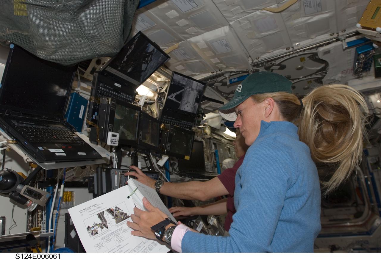 S124-E-006061 (3 June 2008) --- Astronaut Karen Nyberg and Japan Aerospace Exploration Agency (JAXA) astronaut Akihiko Hoshide (partially obscured), both STS-124 mission specialists, work the controls of the International Space Station's robotic Canadarm2 in the Destiny laboratory to maneuver the Kibo Japanese Pressurized Module (JPM) to the port side of the Harmony node.