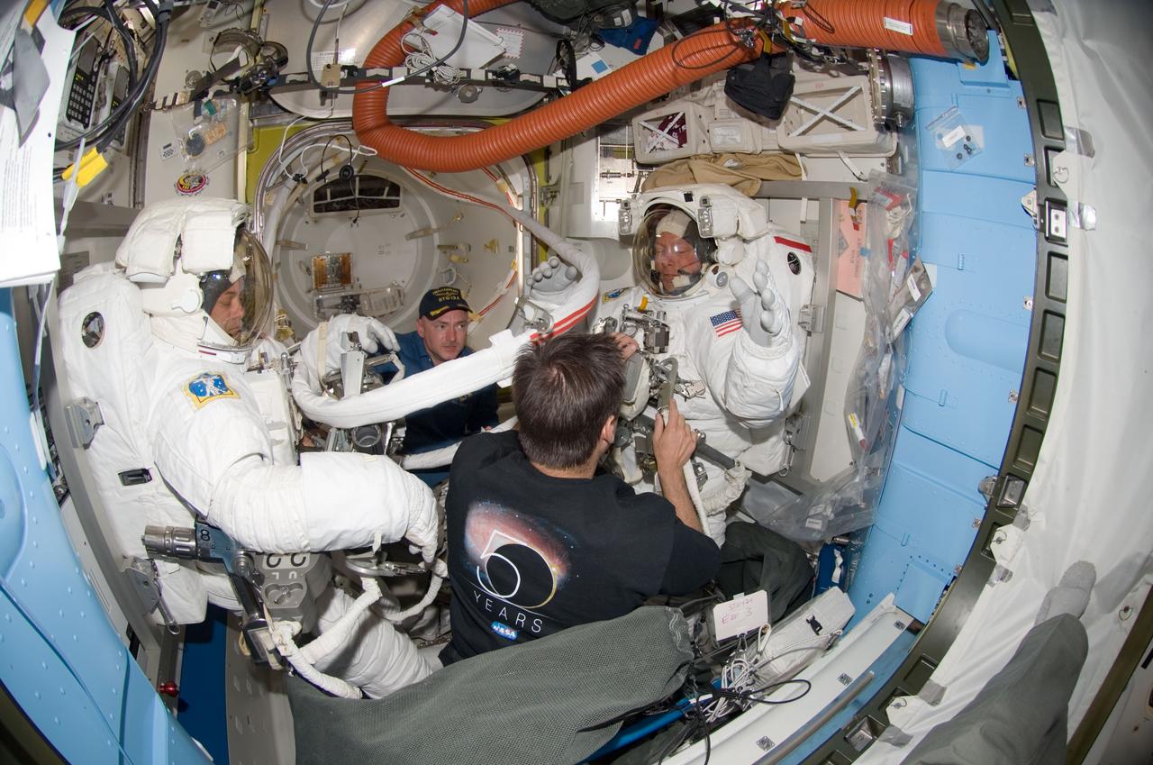 S124-E-007204 (8 June 2008) --- A "fish-eye" lens on a digital still camera was used to record this image of astronauts Ron Garan (left) and Mike Fossum (right), both STS-124 mission specialists, as they prepare for the mission's third scheduled session of extravehicular activity (EVA) in the Quest Airlock of the International Space Station while Space Shuttle Discovery is docked with the station. Astronauts Mark Kelly (background), commander, and Greg Chamitoff, Expedition 17 flight engineer, assisted Garan and Fossum.