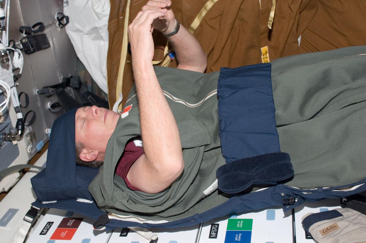 S124-E-007975 (9 June 2008) --- Astronaut Mike Fossum, STS-124 mission specialist, sleeps in his sleeping bag, which is attached to the lockers on the middeck of the Space Shuttle Discovery, while docked with the International Space Station.