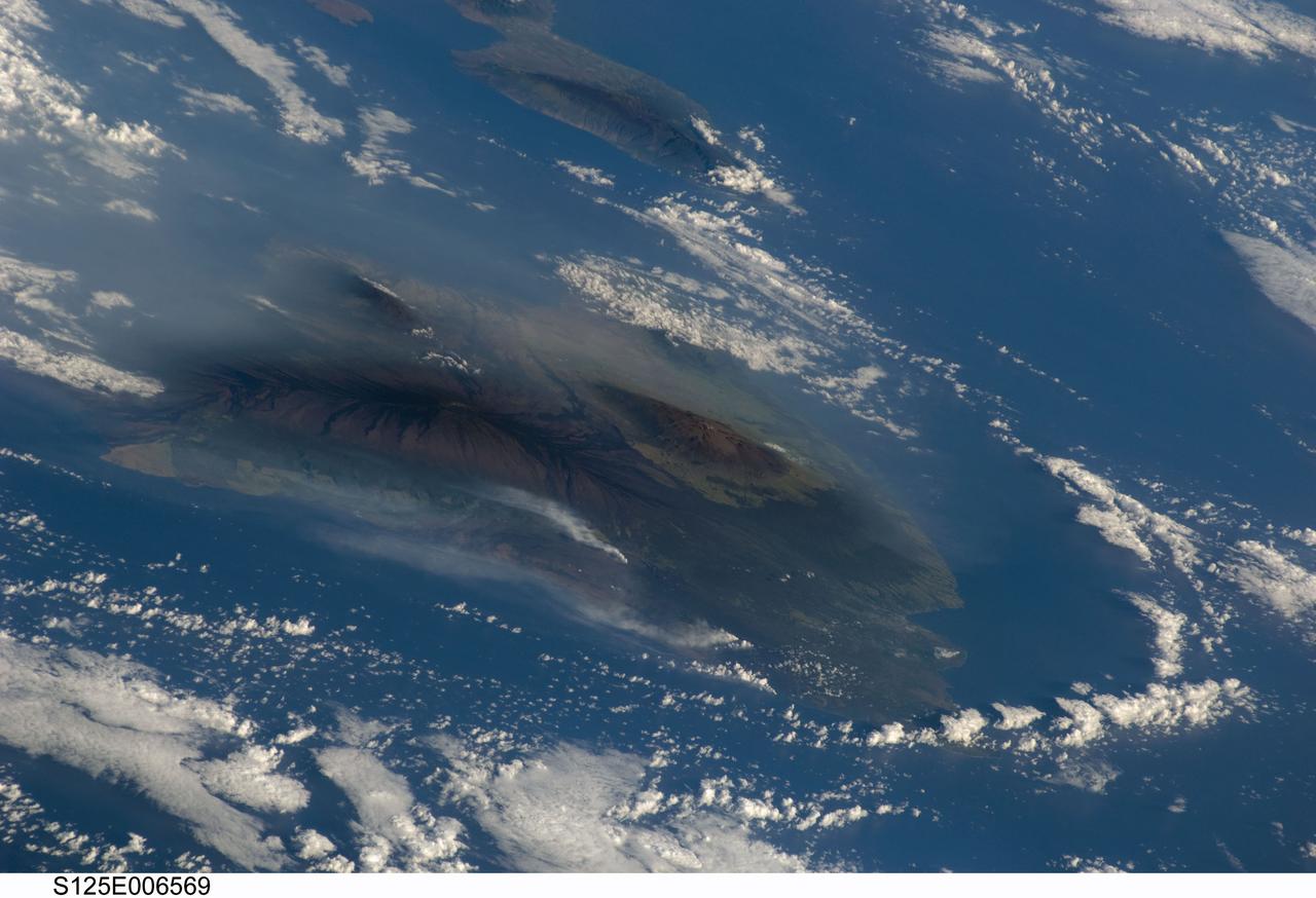 S125-E-006569 (13 May 2009) --- Hawaiian vog from Kilauea volcano, on the island of Hawaii, has been erupting continuously since 1983. This image, taken by the crew of Space Shuttle Atlantis (after completing the capture of the Hubble Space Telescope), shows the volcanic plumes from Kilauea rising up from Halema`uma`u Crater and along the coastline from lava flows entering the ocean from the East rift zone. The volcanic activity has created a blanket of volcanic fog, called vog that envelops the island. The Hawaii Volcano Observatory (HVO) maintains a website (including webcams) that continuously monitors and updates reports on the volcanic activity. Recent maps indicate expanded lava coverage along the coastal plain. In addition, Hawaii?s Department of Health maintains daily vog alerts, and publishes advisories for vog conditions around the ?big island? of Hawaii and the state. When this image was acquired, the region west of Hawaii Volcanoes National Park (downwind from the coastal plumes) had a vog advisory for people with respiratory sensitivities. The Volcano Observatory also reported that ?Lava from east rift zone vents continues to flow through tubes to the coast and is entering the ocean at two locations west of Kalapana. Sulfur dioxide emission rates from the Halema`uma`u and Pu`u `O`o vents remain elevated. Sulfur dioxide emission rates remain elevated and variable; the most recent rate measurement was 1,200 tonnes/day on May 12, compared to the 2003-2007 average rate of 140 tonnes/day. Small amounts of mostly ash-sized tephra continue to be produced consisting mostly of Pele's hair -- irregular pieces of vesicular glass -- and a few hollow spherules.?