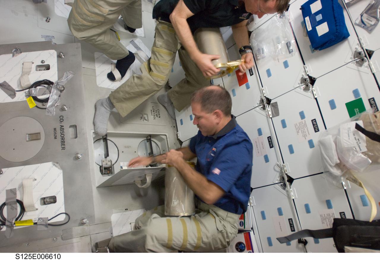 S125-E-006610 (13 May 2009) --- Astronauts John Grunsfeld (bottom), STS-125 mission specialist; and Gregory C. Johnson (partially out of frame), pilot, work with lithium hydroxide (LiOH) canisters from beneath Space Shuttle Atlantis' middeck during flight day three activities.