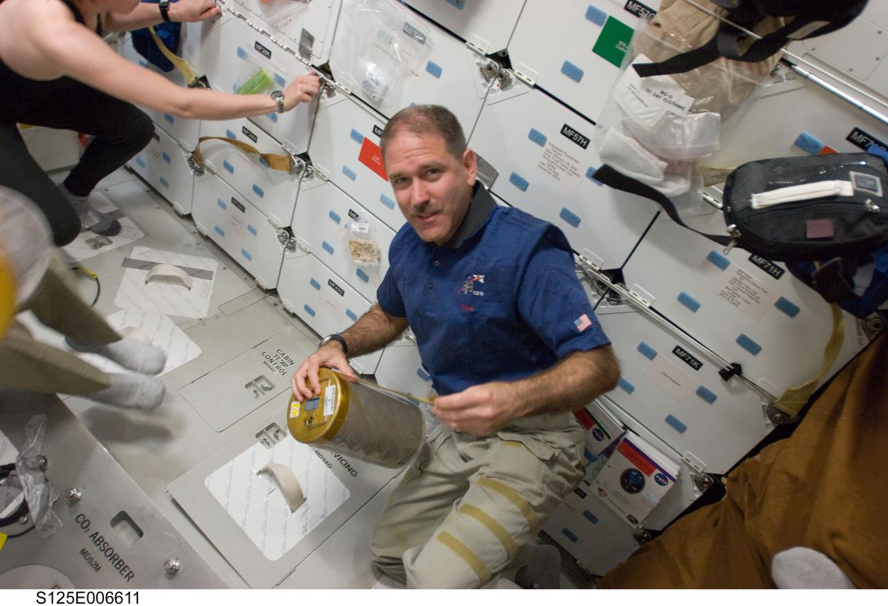 S125-E-006611 (13 May 2009) --- Astronaut John Grunsfeld, STS-125 mission specialist, works with lithium hydroxide (LiOH) canisters from beneath Space Shuttle Atlantis' middeck during flight day three activities.