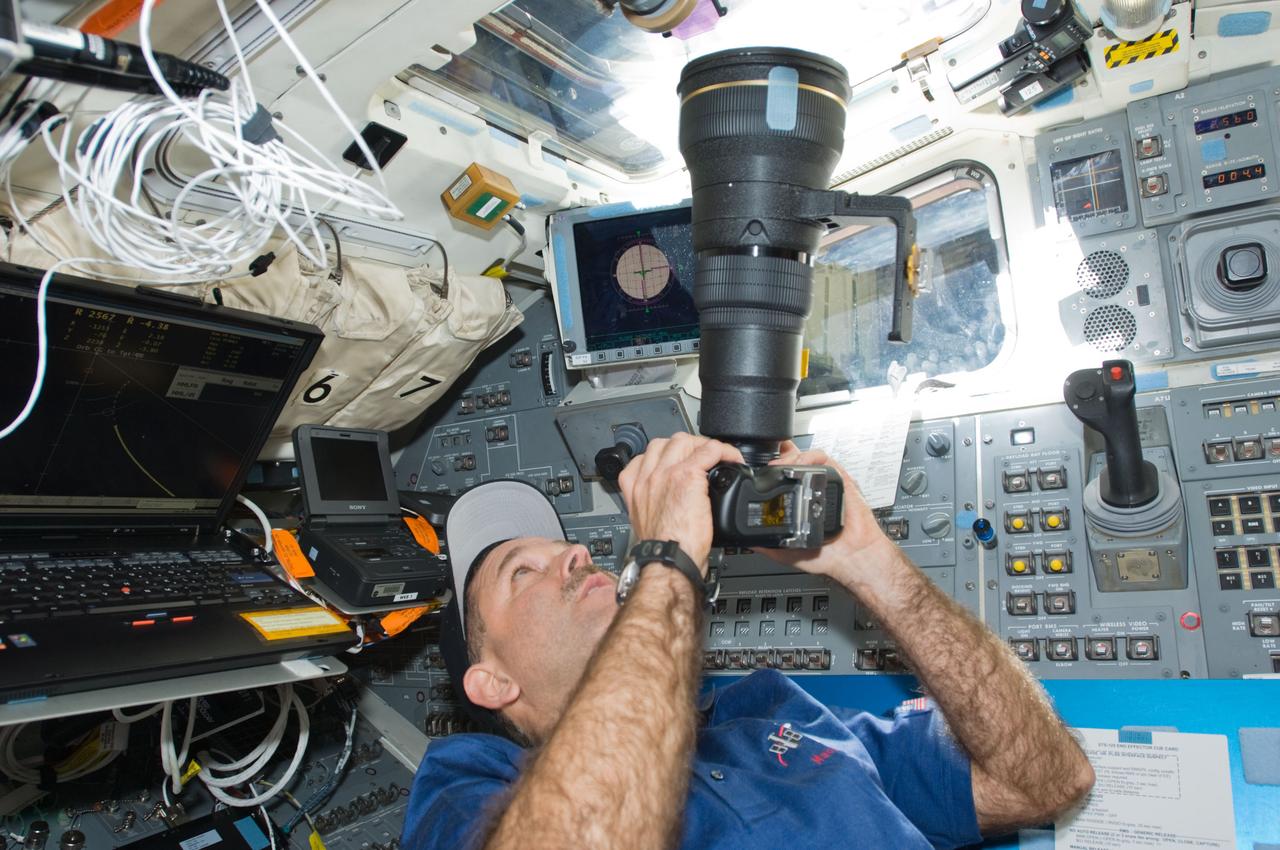 S125-E-006636 (13 May 2009) --- Astronaut John Grunsfeld, STS-125 mission specialist, uses a still camera at an overhead window on the aft flight deck of Space Shuttle Atlantis during flight day three activities.
