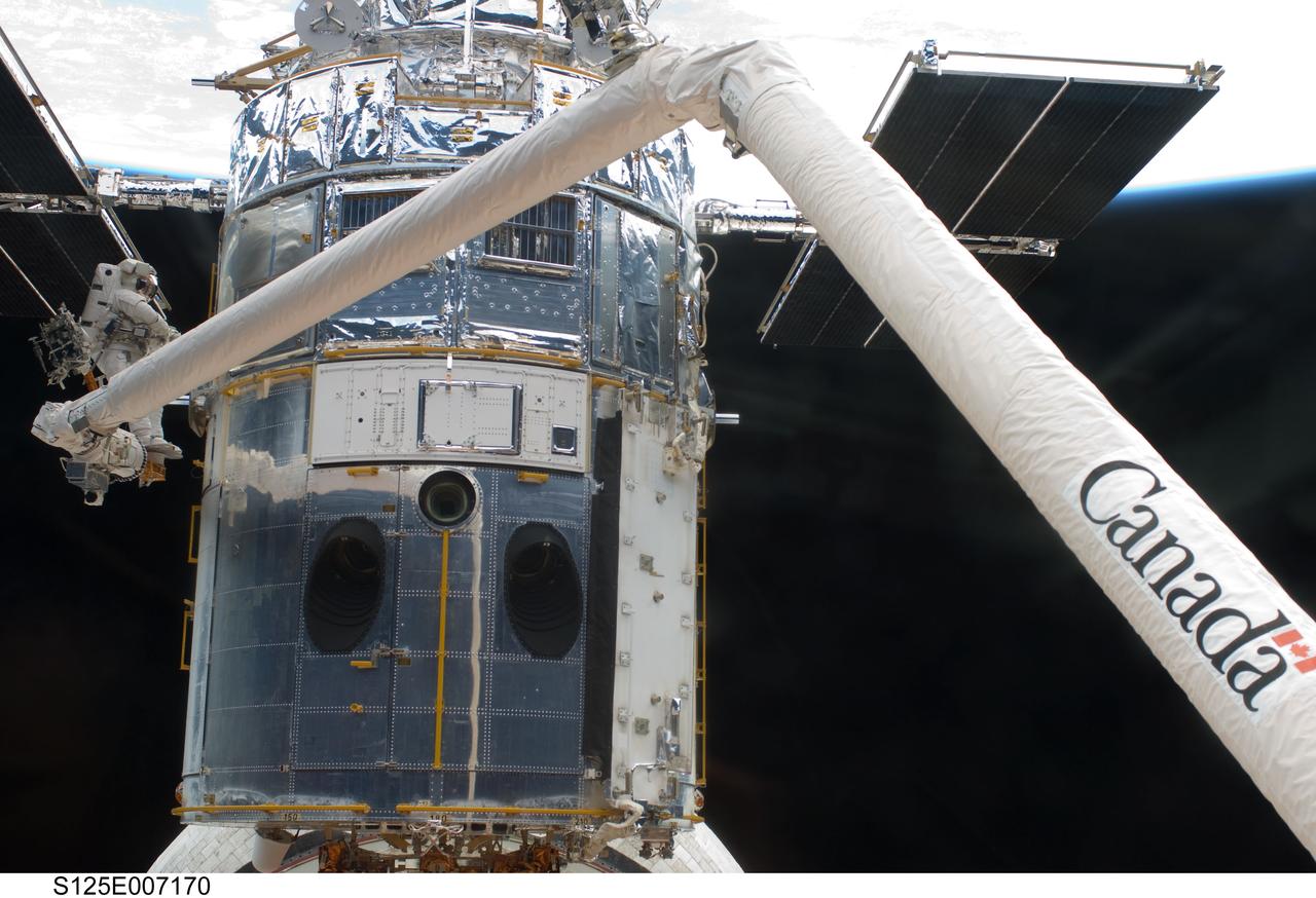 S125-E-007170 (14 May 2009) --- Perched on the end of the Canadian-built remote manipulator system, astronaut Andrew Feustel, mission specialist,  performs work on the Hubble Space Telescope as the first of five STS-125 spacewalks kicks off a week?s work on the orbiting observatory. Feustel, teamed with  astronaut John Grunsfeld (out of frame),  will join the veteran spacewalker on two of the remaining four sessions of extravehicular activity later in the mission.