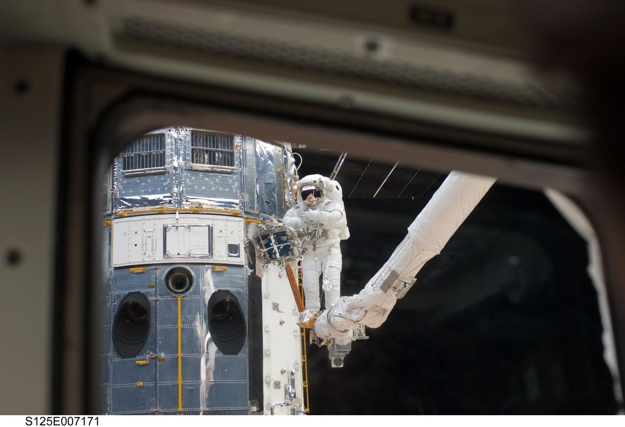 S125-E-007171 (14 May 2009) --- Perched on the end of the Canadian-built remote manipulator system, astronaut Andrew Feustel, mission specialist,  performs work on the Hubble Space Telescope as the first of five STS-125 spacewalks kicks off a week?s work on the orbiting observatory. Feustel, teamed with  astronaut John Grunsfeld (out of frame),  will join the veteran spacewalker on two of the remaining four sessions of extravehicular activity later in the mission.